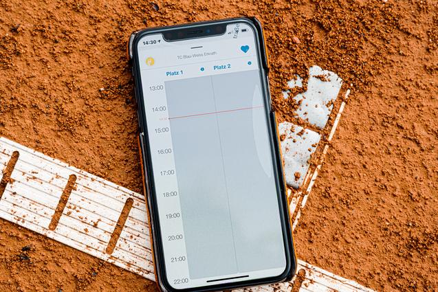 Smartphone auf rotem Tennisplatz, zeigt den Wochenplan mit Zeiten für zwei Plätze.